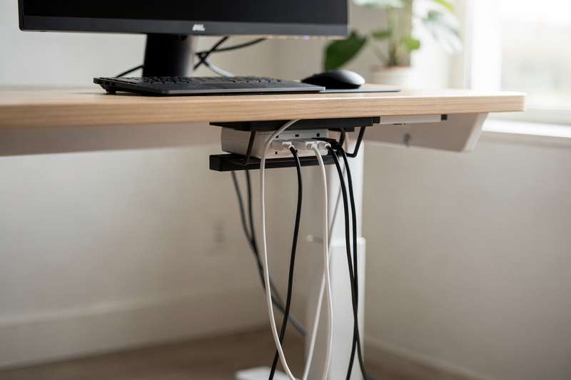 Bundled cables and power cords organized neatly under a standing desk workspace.