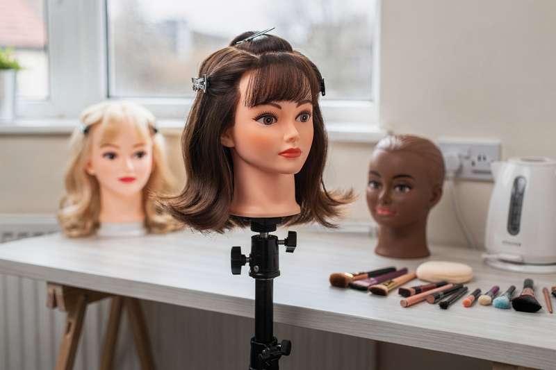 Assorted practice mannequin heads for makeup application and hairstyling training with various skin tones and hair types.