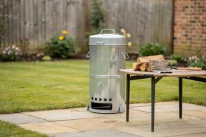 Compact metal garden incinerator with perforated sides standing in a backyard setting.