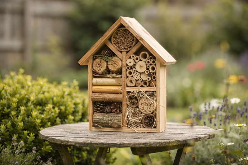 Wooden insect hotel structure with multiple compartments filled with natural materials like straw, bark, and hollow stems.