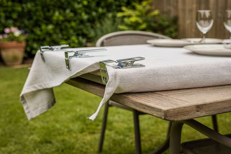 Heavy-duty metal clamps securing a patterned tablecloth on an outdoor garden table during a summer event.