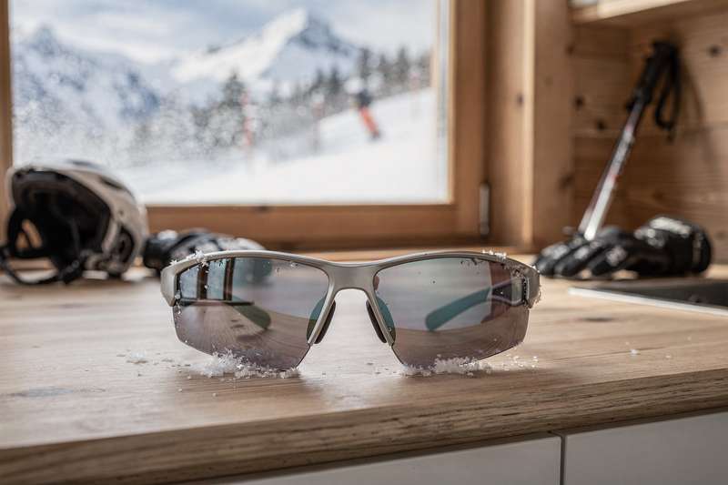 Premium UV400 ski goggles displayed on snowy mountain terrain with bright sunlight reflection.