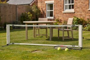 Portable tennis net set up in a UK garden with grass court and boundary lines marked.
