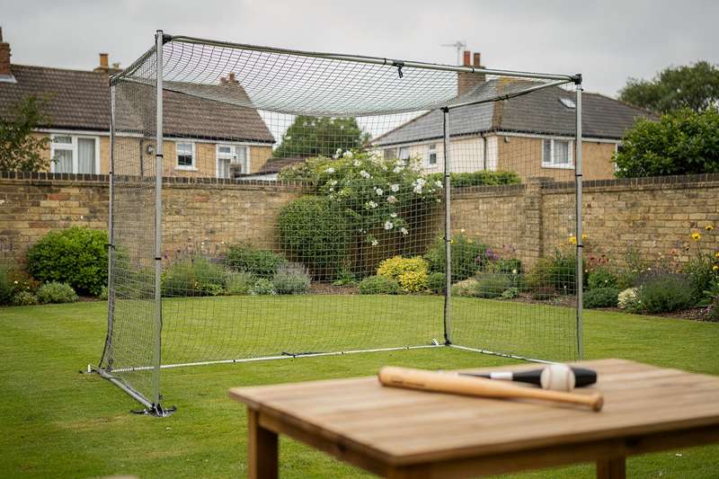 Backyard batting cage setup with netting frame and baseball bat positioned for practice training.